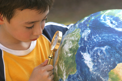 Child holding a magnifying glass up to a globe